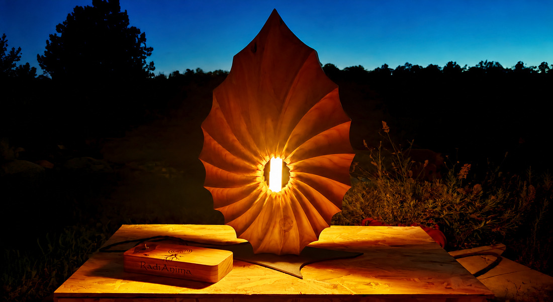 Filo di Luce, scultura in cedro del Libano con selenite illuminata e scatola di comando RadiAnima al crepuscolo.
